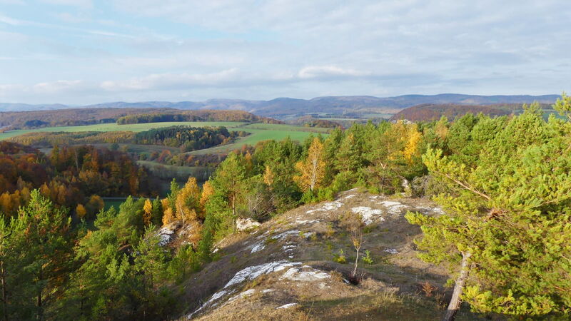 Landschaftsblick in eine Hügellandschaft im Herbst. Im Vordergrund weißes Gipsgestein auf kurzrasiger Hügelkuppe