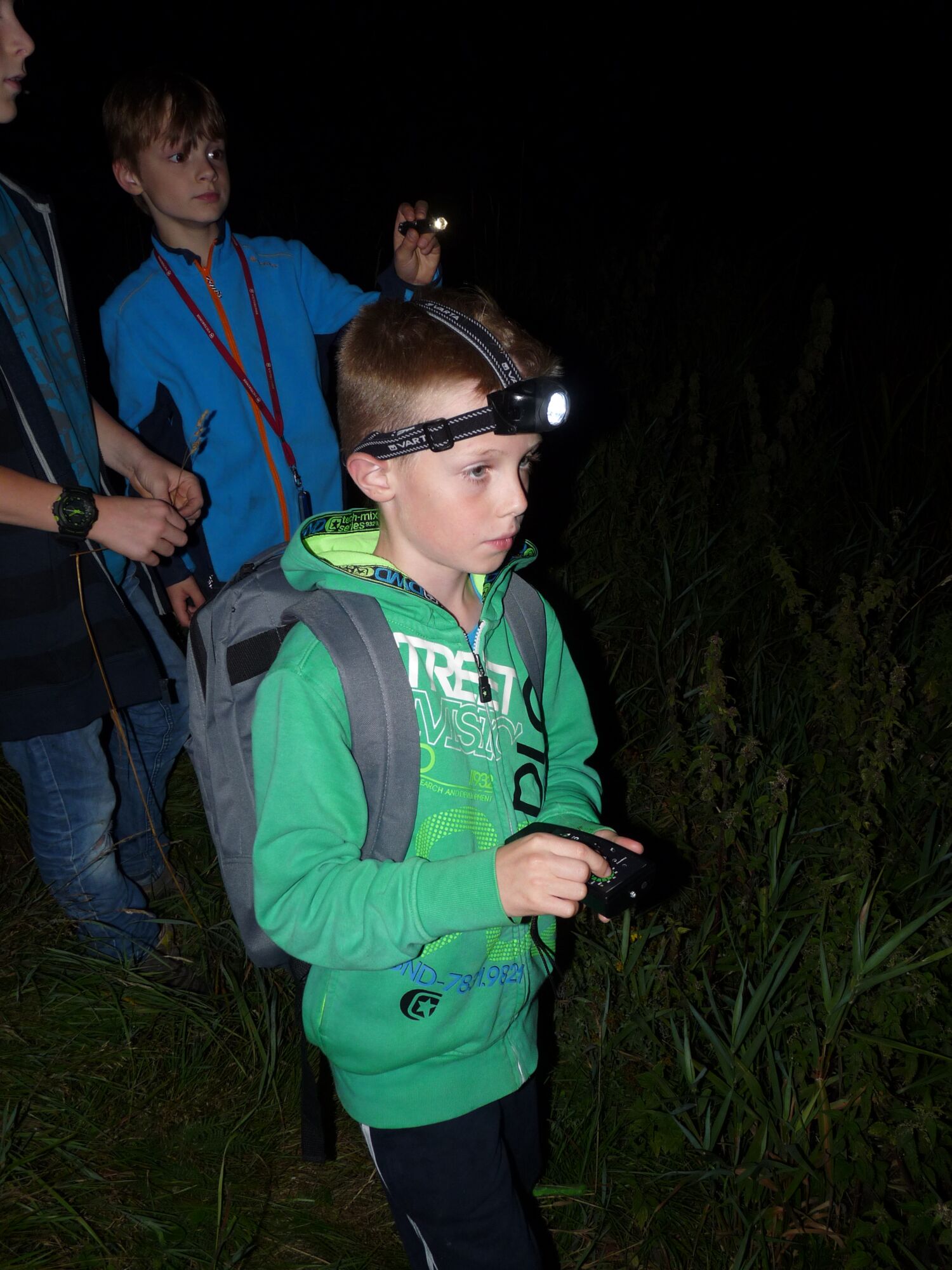ein Junge mit einer Stirnlampe und Rucksack nimmt an einer Fledermausexkursion teil